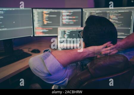 Rear view photo of it specialist guy sitting comfy office chair holding hands behind head looking many monitors testing ip address waiting team Stock Photo