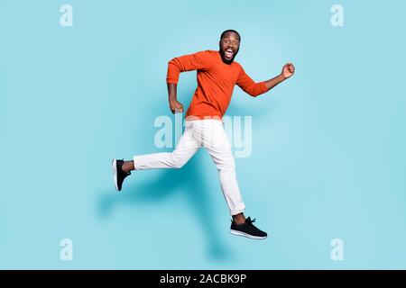 Full length body size photo side profile of man mixed-race expressing positive emotions wearing sneakers white trousers pants running jumping to Stock Photo