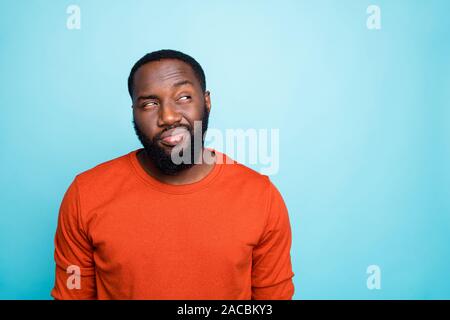 Photo of attractive dark skin guy looking tricky to empty space playful mood think over funny trick wear casual orange sweater isolated blue color Stock Photo