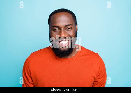 Close up photo of attractive dark skin guy toothy beaming smiling on camera positive mood wear orange jumper isolated blue color background Stock Photo