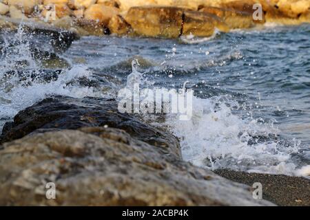 Waves hitting the rocky cliffs in a beach located in Cyprus, Europe, August 2019. Beautiful detailed photo focusing on the waves breaking into drops. Stock Photo