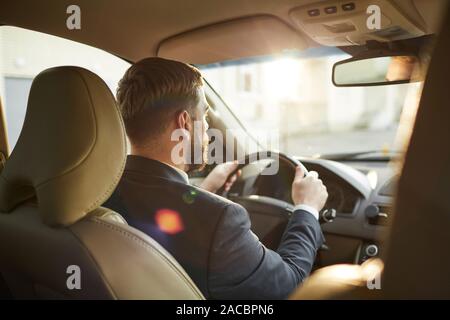 Rear view of young bearded man holding wheel and looking through the windshield and driving Stock Photo