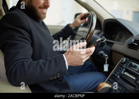 Young man sitting in the car and typing a text messaging on his mobile phone during driving Stock Photo