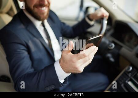 Close-up of young man holding mobile phone in his hand reading a message and smiling while sitting behind the wheel Stock Photo