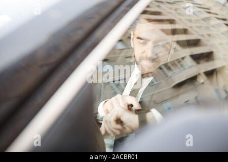 Young businessman sitting in the car and checking the time on the wristwatch Stock Photo