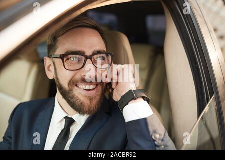 Successful young man in suit laughing while sitting in the car and talking on the phone Stock Photo