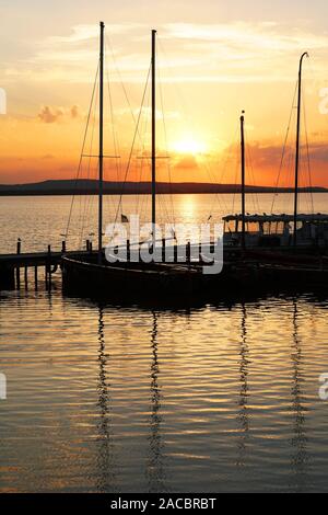 sailboat boats moored at marina pier during sunset sundown over lake Steinhuder Meer in Germany in silhouette Stock Photo