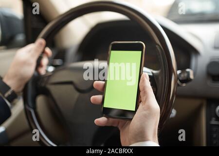 Close-up of young man holding mobile phone with blank screen in his hand he using navigator during driving Stock Photo