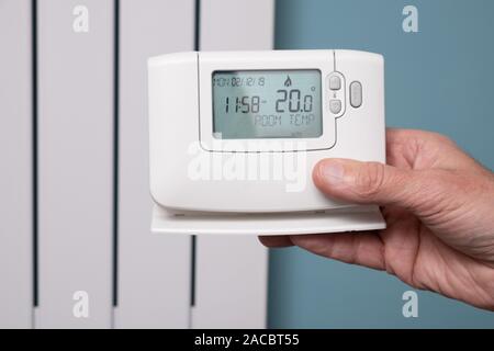 Hand holding central heating controller with modern radiator panel in background Stock Photo