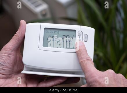 Hand holding central heating controller with modern radiator panel in background Stock Photo