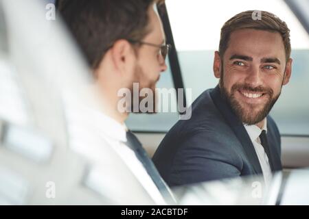 Young happy businessman talking to his colleague and smiling while they sitting in the car Stock Photo