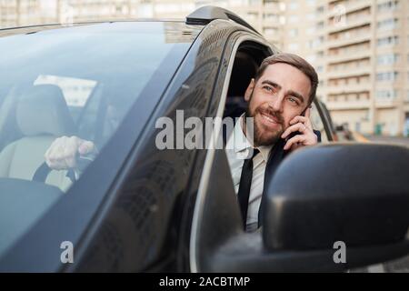 Young happy businessman driving his car leaning out the window and talking on mobile phone Stock Photo