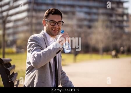 Young businessman is resting and drinking water in park after work. Stock Photo