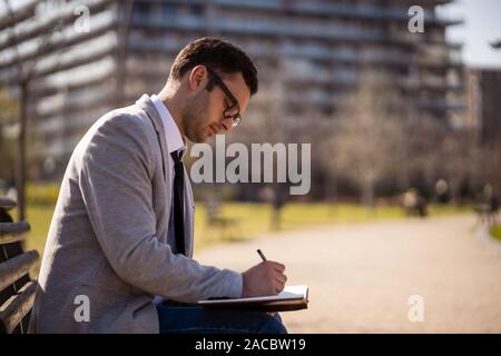 Young businessman is sitting in park and making plans. Stock Photo