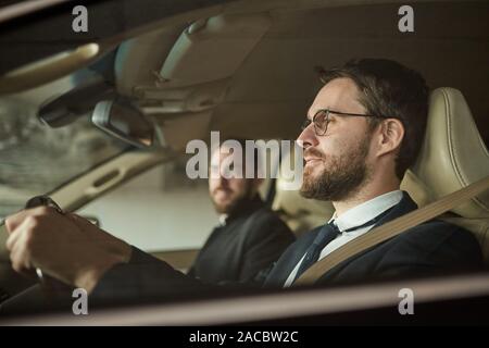 Side view of bearded driver in eyeglasses driving the car with the passenger sitting near by him Stock Photo