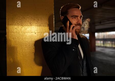Smiling young bearded man has a conversation on mobile phone while standing in the underground parking Stock Photo
