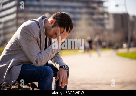 Young businessman is sitting in park after being fired. He is depressed. Stock Photo