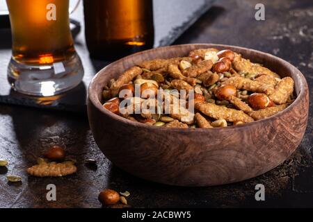 Closeup of a wooden bowl of sesame sticks and nuts with glass and bottle of beer in background Stock Photo