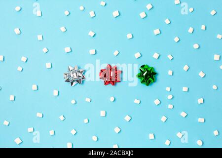 Set of silver red, and gold ribbon satin bows under white marshmallow on light blue background. Minimal winter and Christmas concept. Flat lay. Stock Photo
