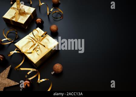 Gift boxes wrapped golden paper and ribbon decorated streamers and baubles on black background. Flat lay.  Christmas and New Year holidays concept. Co Stock Photo