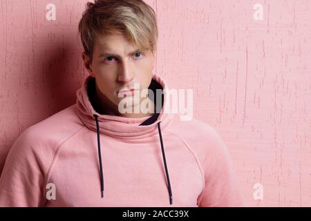 Young man in a pink hoodie on a pink background, portrait of a young stylish guy. Stock Photo