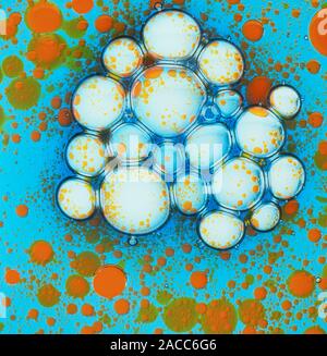 Variation in the molecular properties of different liquids, illustrated by orange dyed water droplets on a background of two stroke oil (blue). The wh Stock Photo
