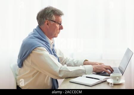 Elderly Businessman Working On Laptop Sitting In Office, Side View Stock Photo