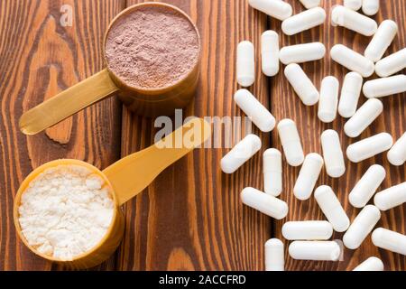 capsules of creatine and protein measuring spoons on a wooden background Stock Photo
