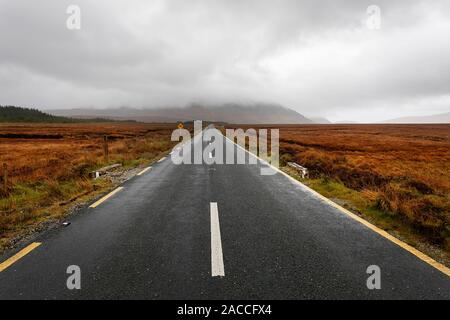 Empty road leading to coastline and islands in a distance, moody dark sky with stormy clouds Stock Photo
