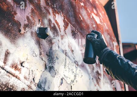 Homeless man spray painting old train wagon with aerosol can. Unrecognizable male person hand close up in conceptual image with selective focus. Stock Photo