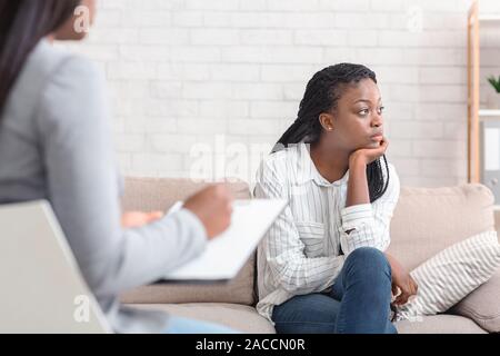 Thoughtful african american woman sitting on couch at psychotherapist's office Stock Photo