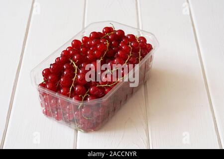 redcurrants fruit in transparent plastic container on white wood table Stock Photo