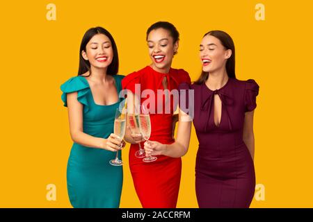 Three Women In Dresses Clinking Champagne Glasses Celebrating, Studio Shot Stock Photo