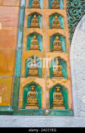 A wall adorned with many oriental golden statues, China. Stock Photo