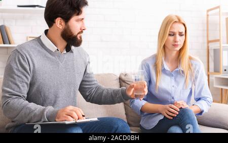Psychologist offering glass of water to crying depressed woman Stock Photo