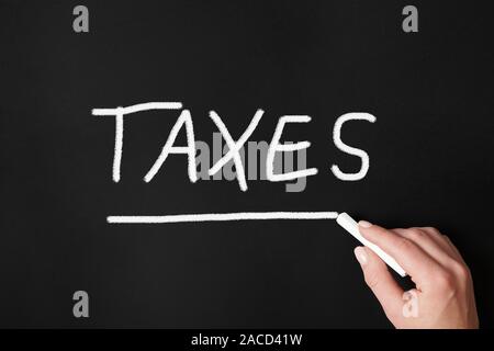female hand writing word taxes with chalk on chalkboard or blackboard - tax concept Stock Photo
