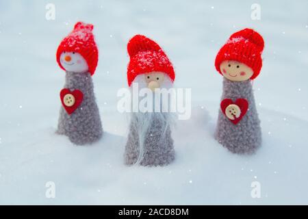 Three dolls gnome in red caps on the background of snow. Christmas miracles Stock Photo
