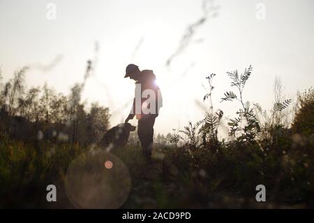 Silhouette of a man with a dog on a walk. Border Collie in the meadow against the rays of the setting sun. Stock Photo