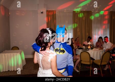 A groom dressed as Batman having fun with his new wife during their first dance, traditional wedding celebration, fun, funny dance, humour Stock Photo