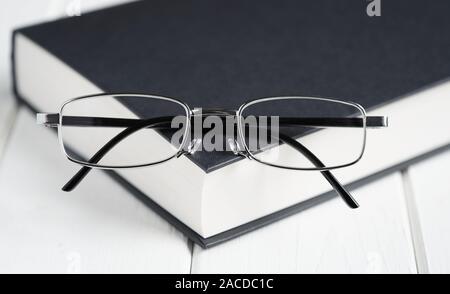 reading glasses or spectacles on top of hardcover book - education and knowledge concept - selective focus with shallow deph of field Stock Photo