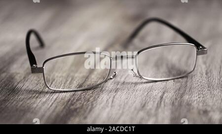 Pair of modern reading glasses or spectacles on rustic wooden table - selective focus with shallow deph of field Stock Photo