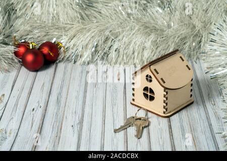 Toy wooden house and two keys on a wooden table decorated with a garland and red Christmas balls for the New Year or XMAS Stock Photo