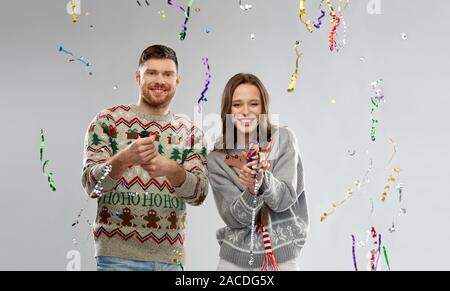 couple in christmas sweaters popping party poppers Stock Photo