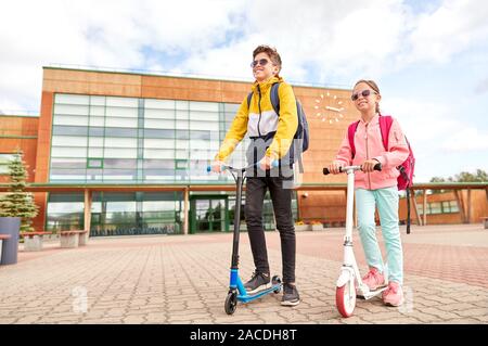 happy school children with backpacks and scooters Stock Photo