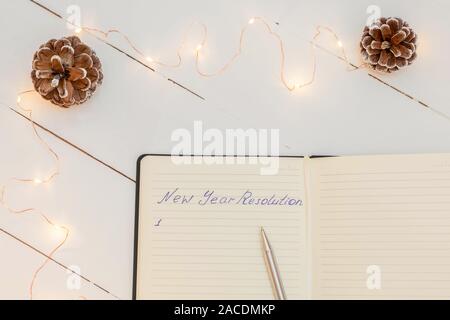 Notepad with handwritten text "New Year Resolution" on white wooden table and Christmas decorations Stock Photo