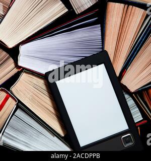 The e-book with a white screen lies on the open multi-colored books that lie on a dark background, close-up Stock Photo