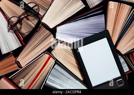 The e-book with a white screen lies on the open multi-colored books that lie on a dark background, close-up Stock Photo