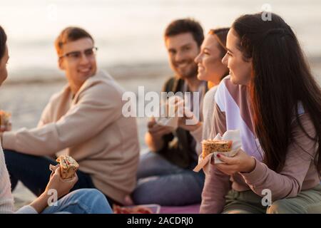 happy friends eating sandwiches at picnic on beach Stock Photo