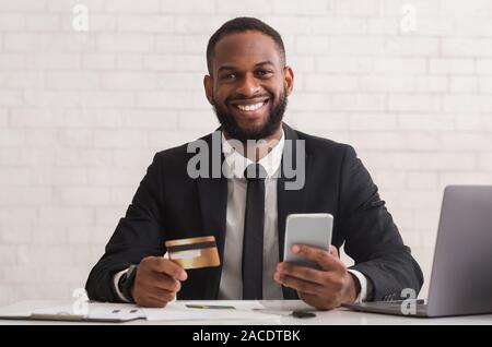 Cheerful afro man holding credit card, making purchases online Stock Photo