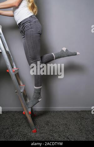 unrecognizable woman climbing and balancing on ladder in socks - home improvement diy or household accident proneness concept Stock Photo